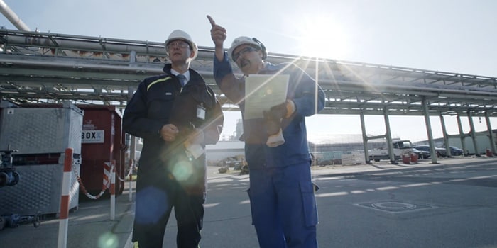 Dos operarios en un polígono industrial examinan sistemas de fluidos.