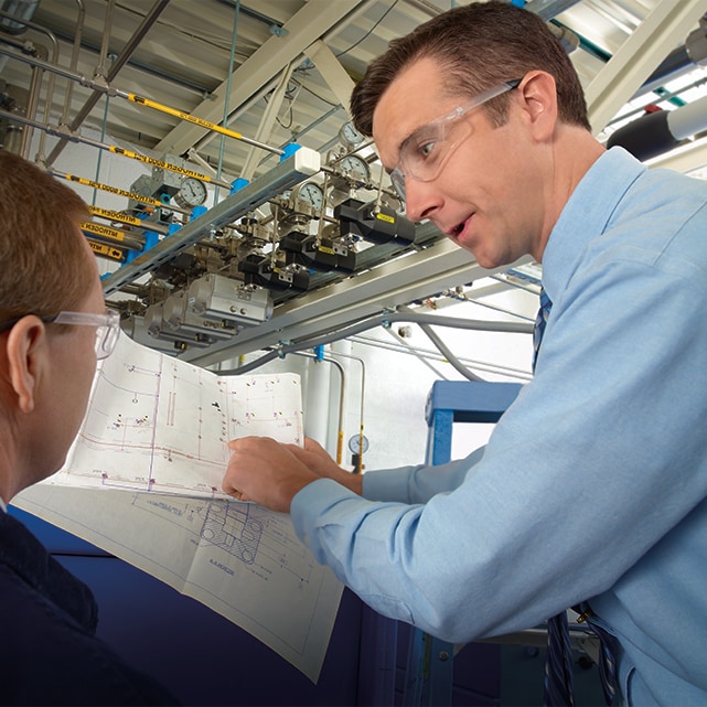 Associates collaborating in a facility while looking at P&IDs with fluid systems in background