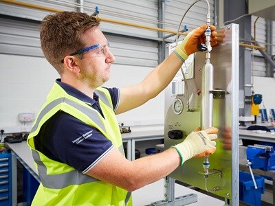 Swagelok technician demonstrating a grab sampling technique, collecting a sample of fluid from a pipeline for analysis in industrial applications.