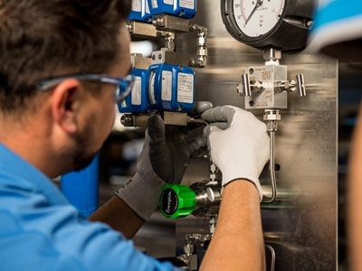 A Swagelok-certified technician assembling a complex fluid system panel with stainless steel tubing and fittings in a workshop setting.