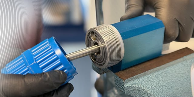 Close‑up of a fluid system fitting being worked on with a precision tool in a workshop environment