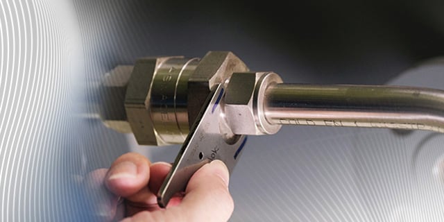 A hand using a tube to measure an installed Swagelok tube fitting