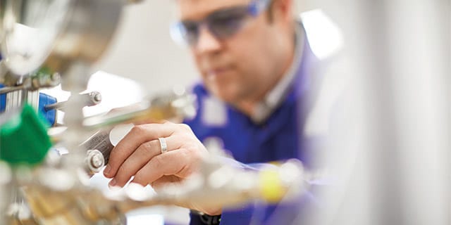 Technician adjusting industrial fluid system equipment in a semiconductor manufacturing environment.