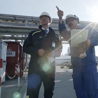 Two men standing in an industrial yard examining fluid systems.